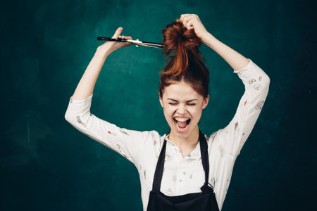 emotional woman in black apron scissors cuts her hairの写真素材