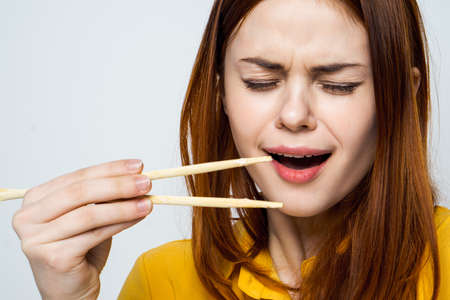 woman eating sushi with japanese chopsticks posing light backgroundの写真素材