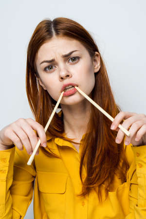 woman eating sushi with japanese chopsticks posing light backgroundの写真素材