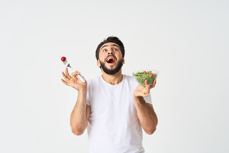 Cheerful man in a white T-shirt with a plate of light green and a healthy meal