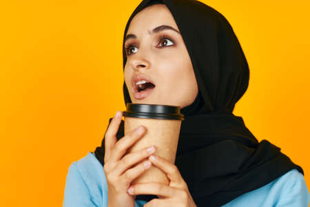 woman in black hijab glass with a drink emotion relaxation yellow backgroundの写真素材