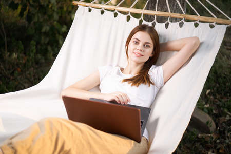woman outdoors with laptop lies in hammock leisure technologyの写真素材