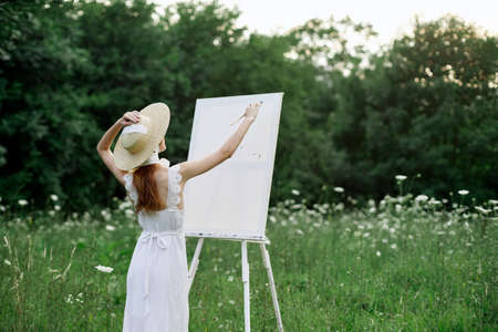 A woman in a white dress in a field with flowers paints a pictureの写真素材