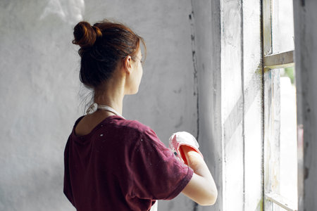 Woman in a white apron paints a window in a house interior renovationの写真素材