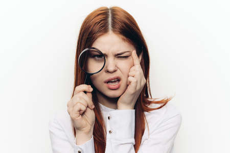 cheerful red-haired woman holding a magnifying glass near her faceの写真素材