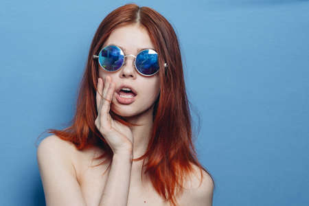 perky red-haired woman in blue glasses bare shoulders posingの写真素材