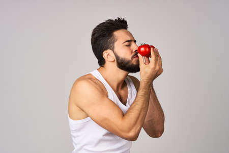 a man in a white t-shirt tomatoes in hand fresh vegetables health light backgroundの写真素材