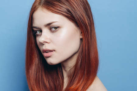 attractive woman with bare shoulders red hair close-up blue backgroundの写真素材