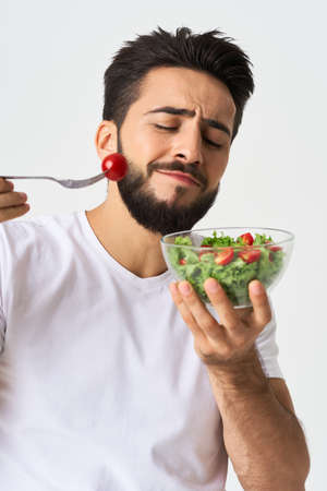Cheerful man in a white T-shirt with a plate of light green and a healthy mealの写真素材
