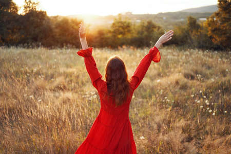 woman in red dress in the field with hands raised up posingの写真素材