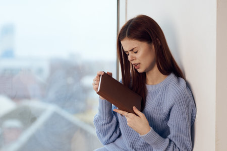 woman reading a book near the window with a cup of drink rest