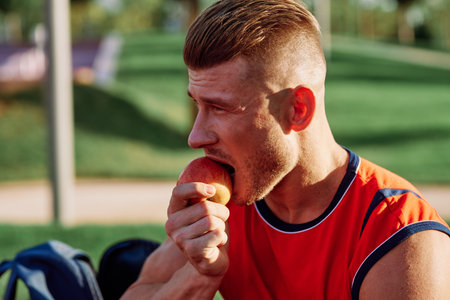 man in the park sits on a bench and eats an apple summer