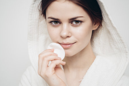 woman with a hood on her head wipes her face with a cotton pad skin careの写真素材