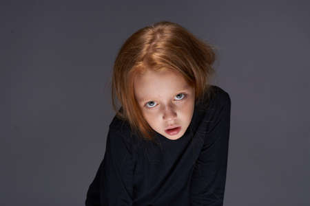 red-haired girl with freckles on her face in a black sweater posingの写真素材