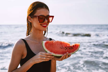 cheerful woman in sunglasses eating watermelon by the oceanの写真素材