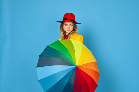 woman in yellow coat multicolored umbrella posing blue backgroundの写真素材