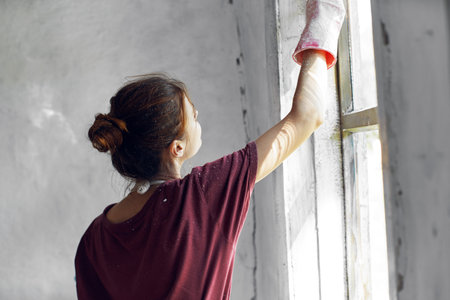 Woman in a white apron paints a window in a house interior renovationの写真素材