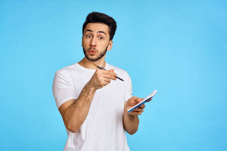 man in white t-shirt notebook with pen student blue backgroundの写真素材