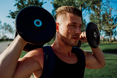 athletic man with dumbbells in his hands in the park training lifestyle