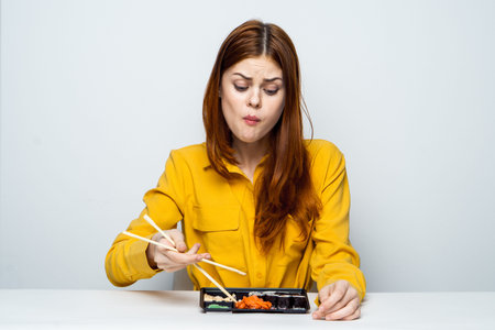 a woman in a yellow shirt sits at a table and eats sushi