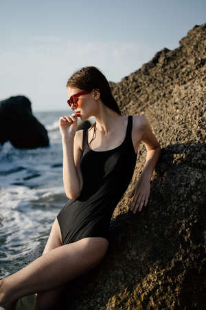 woman in swimsuit sunglasses ocean rocks posingの写真素材