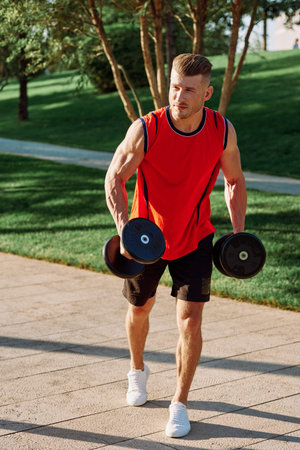 athletic man with dumbbells in his hands outdoors in the park