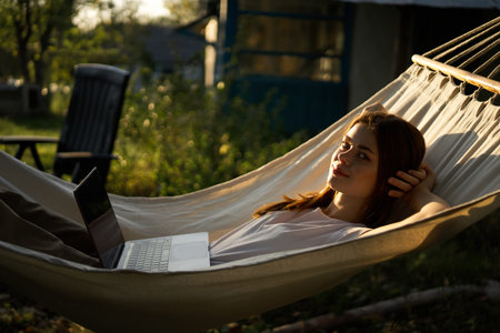 woman lies in a hammock with laptop on nature vacation travel
