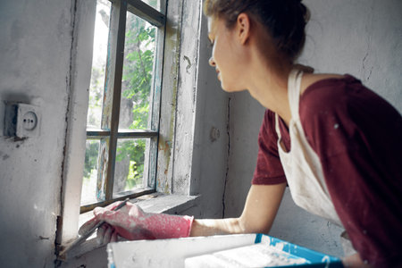 woman painter makes home repairs near window interior