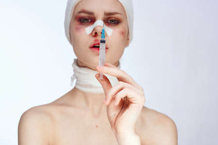 emotional woman with bandaged face bruises syringe in hand painkillers isolated backgroundの写真素材