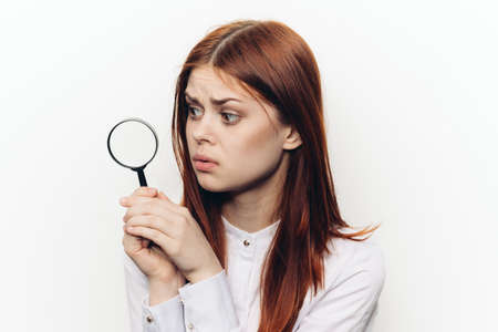 cheerful red-haired woman holding a magnifying glass near her faceの写真素材