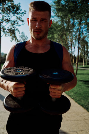 athletic man with dumbbells in his hands in the park training lifestyleの写真素材