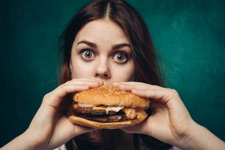 cheerful woman with hamburger near face snacking fast foodの写真素材
