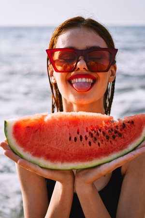 cheerful woman in sunglasses eating watermelon by the oceanの写真素材