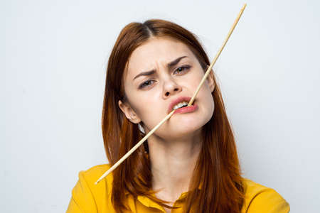 woman eating sushi with japanese chopsticks posing light backgroundの写真素材