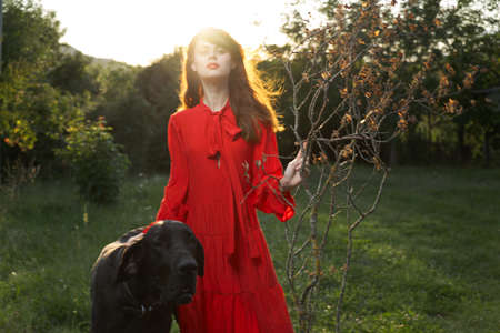 beautiful woman in a red dress outdoors with a black dog friendshipの写真素材