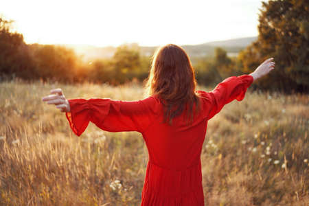 woman in red dress in the field with hands raised up posingの写真素材