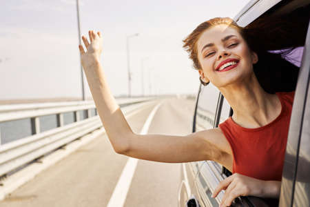 cheerful woman peeking out of the car window trip road travelの写真素材