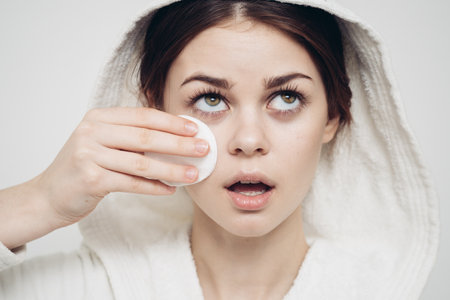 woman with a hood on her head wipes her face with a cotton pad skin careの写真素材