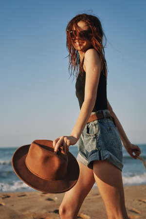 cheerful woman in a hat with sunglasses walking with a bagの写真素材