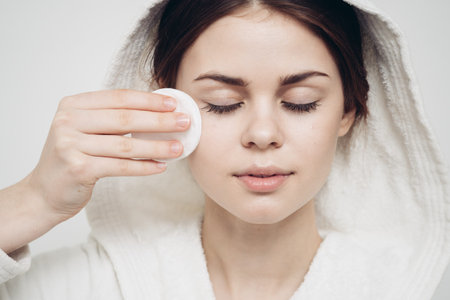 woman with a hood on her head wipes her face with a cotton pad skin care