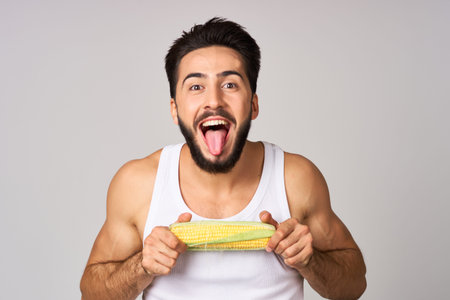 a man in a white t-shirt with corn in hand fresh vegetables health studio lifestyle