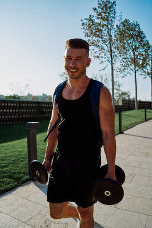 athletic man with dumbbells in his hands in the park training lifestyle