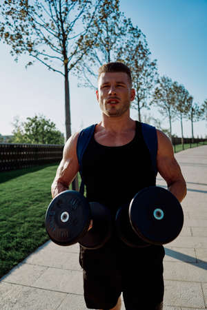 athletic man with dumbbells in his hands in the park training lifestyleの写真素材