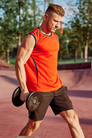 male athlete with dumbbells in hands training in the parkの写真素材