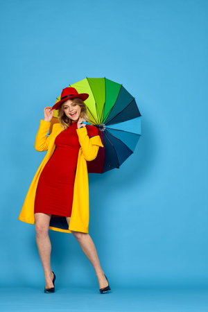 woman in yellow coat multicolored umbrella posing blue backgroundの写真素材
