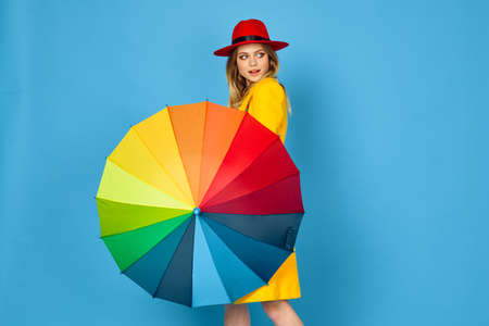 woman in yellow coat multicolored umbrella posing blue backgroundの写真素材