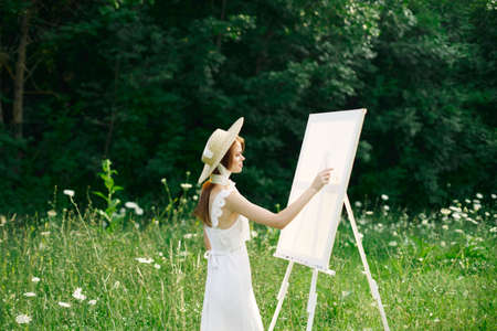 Woman in white dress in nature paints a picture of a landscape hobbyの写真素材