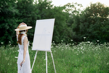 A woman in a white dress in a field with flowers paints a pictureの写真素材