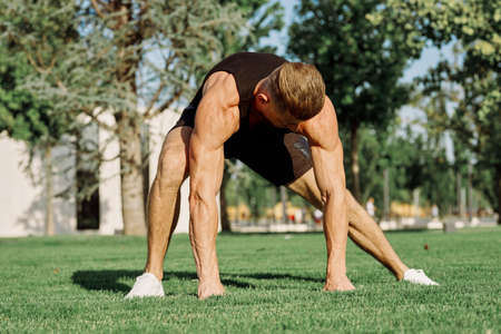 sports man doing exercises on the lawn in the parkの写真素材