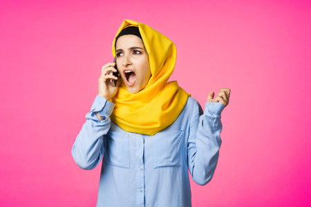 muslim woman in yellow hijab talking on the phone technology pink background
